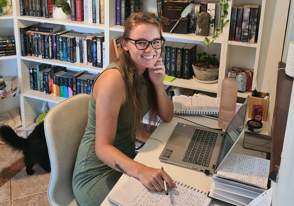 Author Madeline Te Whiu working at her desk, surrounded by editorial notes and bookcases.